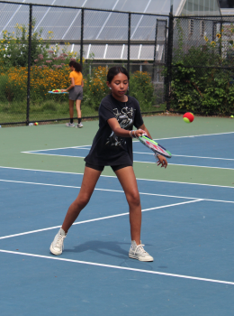 Girl swinging a tennis racket on a blue court.